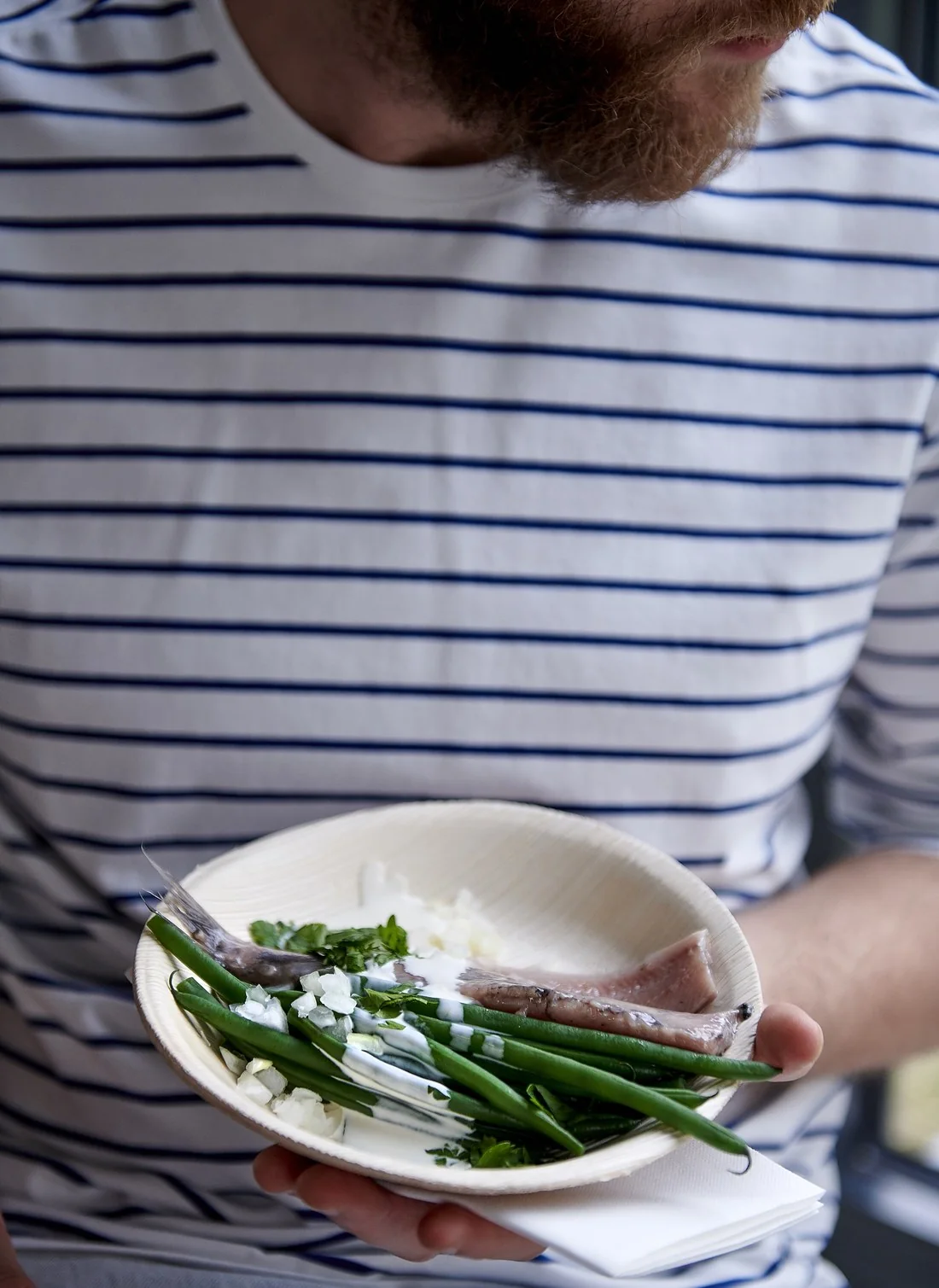 Shot on set: a bearded man in a striped shirt holds a plate of herring with green beans